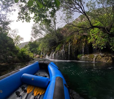 A raft boat gently floats close to stunning waterfalls along the Cetina River, showcasing the natural beauty of Croatia’s rugged landscape. Raft boat floating near cascading waterfalls on the Cetina River