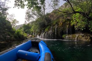 A raft boat gently floats close to stunning waterfalls along the Cetina River, showcasing the natural beauty of Croatia’s rugged landscape. Raft boat floating near cascading waterfalls on the Cetina River