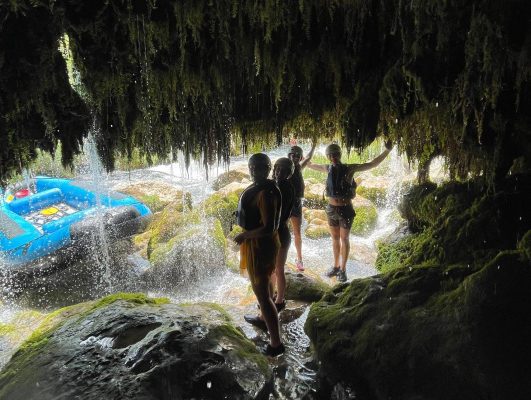 Rafting group taking a refreshing break in a cave beneath a cascading waterfall along the Cetina River. Group resting inside a cave under a waterfall during rafting on the Cetina River