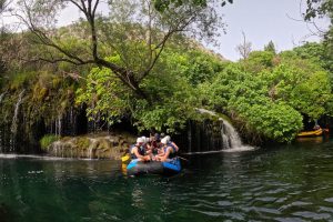 Rafting grupa uživa u osvježavajućem odmoru ispod slapova na rijeci Cetini. Grupa odmara ispod slapova tijekom raftinga na rijeci Cetini