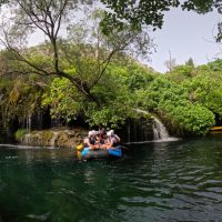 A group of rafters navigating the clear, turquoise waters of the Cetina River surrounded by lush green cliffs near Split. Rafting adventure on the Cetina River near Split, Croatia