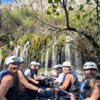 Skupina sudionika nasmijano pozira pored rafting čamca Prijatelji se fotografiraju uz čamac na rijeci Cetini