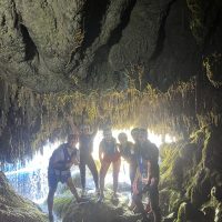 A group of tourists enters a cave during the rafting trip, wearing helmets and life jackets. Rafting participants exploring a cave by the Cetina River