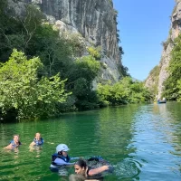 A cheerful team in a boat rides down the rapids surrounded by greenery. Group of friends swimming in a Cetina River near Omiš city