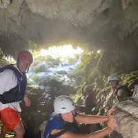 Grupa turista ulazi u špilju tijekom rafting izleta, noseći kacige i prsluke Family in the cave under a waterfall