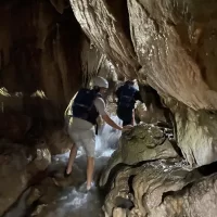 Rafteri istražuju skrivenu špilju u stijenama uz rijeku, osvijetljenu prirodnim svjetlom. Friends explorng stunning cave on a Cetina rafting tour