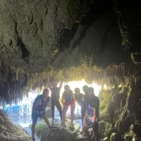 A group of tourists enters a cave during the rafting trip, wearing helmets and life jackets. Friends taking picture in a cave with stalactites