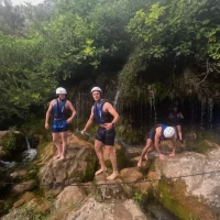 A calm and peaceful section of the Cetina River glowing with warm sunset colors, as rafters gently float downstream. Party posing, and excited near cave entrance