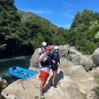 Ekipa pozira s osmijesima i veslima nakon završene rafting avanture. Rafting crew smiling o a shore after rafting tour