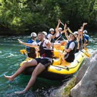 Smiling rafters enjoying the sunny weather while drifting on the serene parts of the Cetina River surrounded by nature. Group of friends enjoying a sunny day rafting on the Cetina River