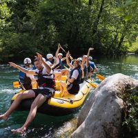 Smiling rafters enjoying the sunny weather while drifting on the serene parts of the Cetina River surrounded by nature. Group of friends enjoying a sunny day rafting on the Cetina River